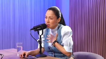 Katy Jara, con el cabello recogido y vestida con una blusa blanca y chaleco de mezclilla, llora mientras habla en un micrófono Shure en un estudio