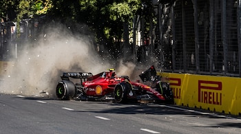 Un auto de carreras rojo impacta contra un muro amarillo, levantando una cortina de polvo y fragmentos de su carrocería sobre el asfalto.