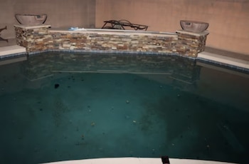 Piscina exterior de noche con agua oscura, delimitada por un muro de piedra con dos cuencos ornamentales en la parte posterior
