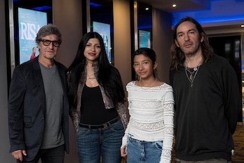 Cuatro personas posan de pie frente a carteles de cine. Incluyen un hombre con gafas, una mujer de cabello oscuro, una niña y un hombre con cabello largo