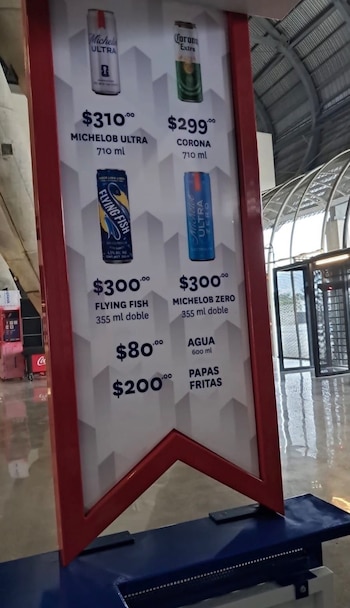 Panel con precios de bebidas y snacks en un evento deportivo: cervezas Michelob Ultra, Corona, Flying Fish, Michelob Zero, agua y papas fritas con sus costos