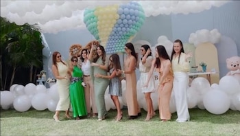 Ocho mujeres posan en un jardín decorado con globos blancos en el suelo y una figura de globo aerostático hecha con globos pastel