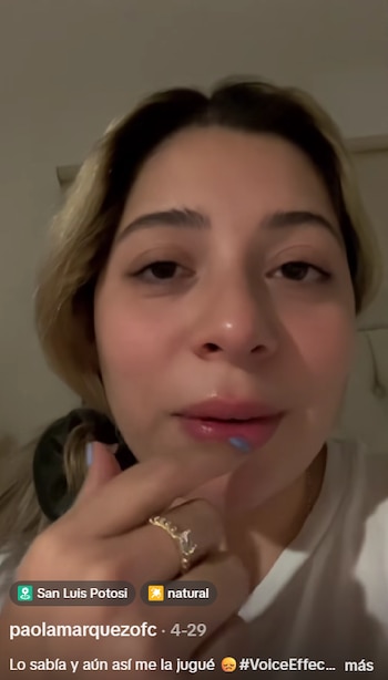 Primer plano de una joven mujer de cabello rubio, mirando hacia el frente, con un anillo de compromiso visible en su dedo mientras toca sus labios