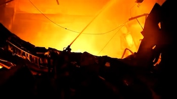 Un chorro de agua apaga un gran fuego entre escombros oscuros y restos de estructuras metálicas colapsadas
