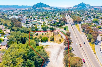 Terreno con línea roja, una autopista con vehículos, edificios residenciales, árboles frondosos y montañas bajo un cielo despejado