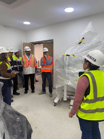Un grupo de personas con cascos blancos de seguridad y chalecos reflectantes observa un equipo cubierto con un plástico transparente