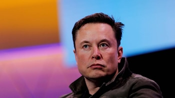 Primer plano de Elon Musk, hombre de cabello oscuro, mirando a la derecha. Viste chaqueta oscura. Fondo borroso con degradados de naranja, morado y azul