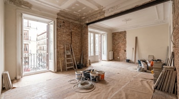 Interior de un piso antiguo en Madrid en reforma. Paredes de ladrillo visto, techos con molduras, suelo de madera protegido. Herramientas y materiales de obra.