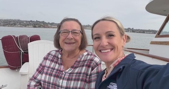 Dos mujeres sonríen a cámara en la cubierta de un barco. Una mujer mayor con gafas y camisa a cuadros y una mujer joven con pelo rubio y chaqueta azul