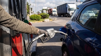 Mano sosteniendo la boquilla de una manguera de surtidor para cargar gasolina en un automóvil azul estacionado.