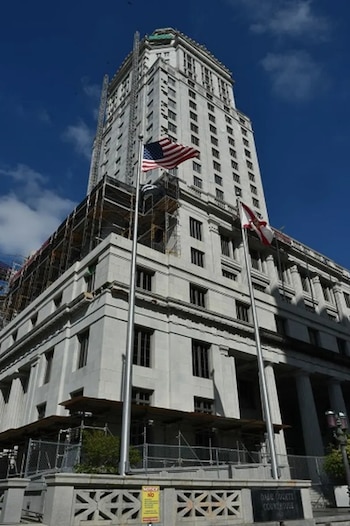 Un edificio alto de piedra clara con andamios en sus pisos inferiores y dos astas con las banderas de Estados Unidos y de Florida al frente