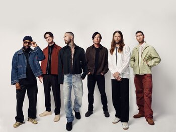 Seis hombres, los miembros de Maroon 5, posan de pie sobre un fondo blanco con ropa casual de diversos estilos y colores
