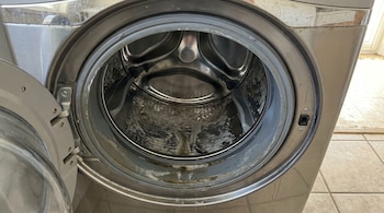Um close do tambor da máquina de lavar está aberto pela frente, mostrando o interior de metal e a sujeira visível na vedação de borracha.