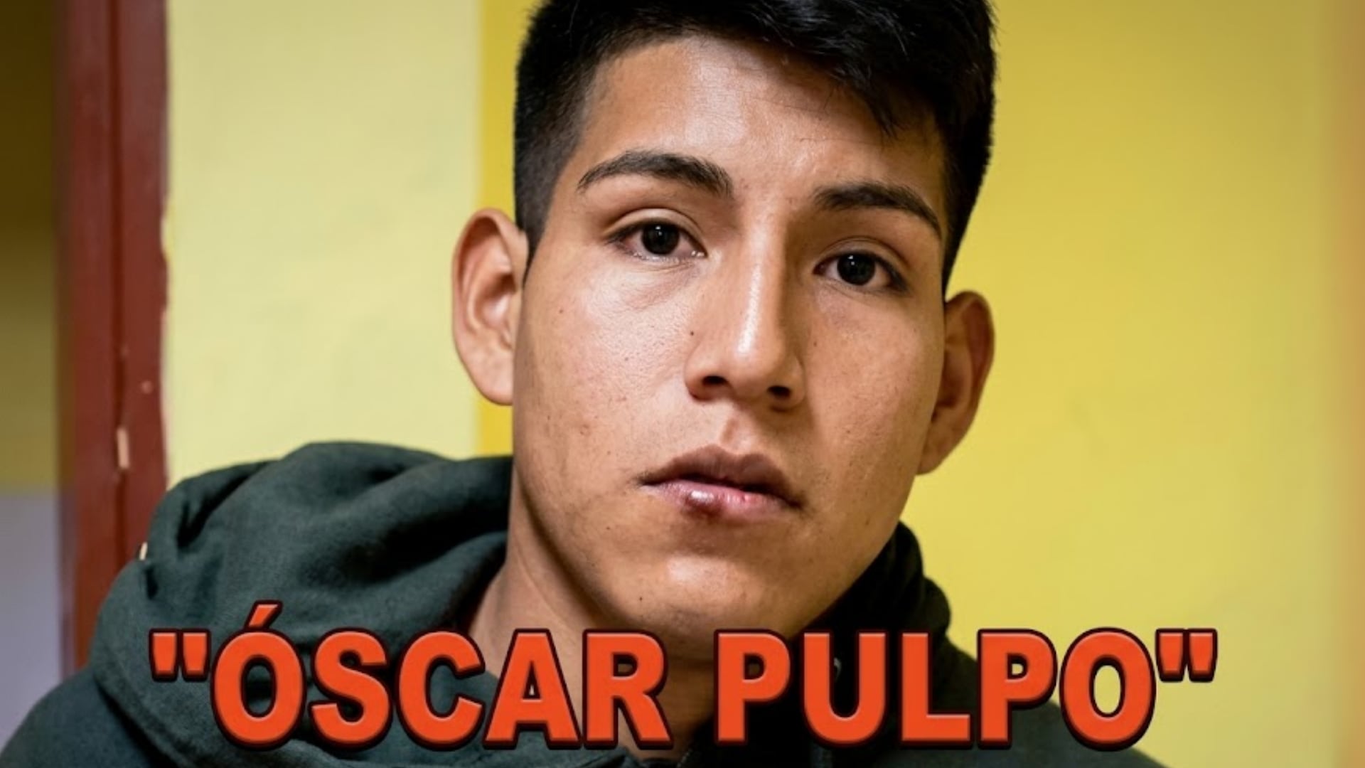Un joven identificado como Óscar Pulpo mira fijamente a la cámara frente a una pared de tono amarillo. (Infobae Perú)