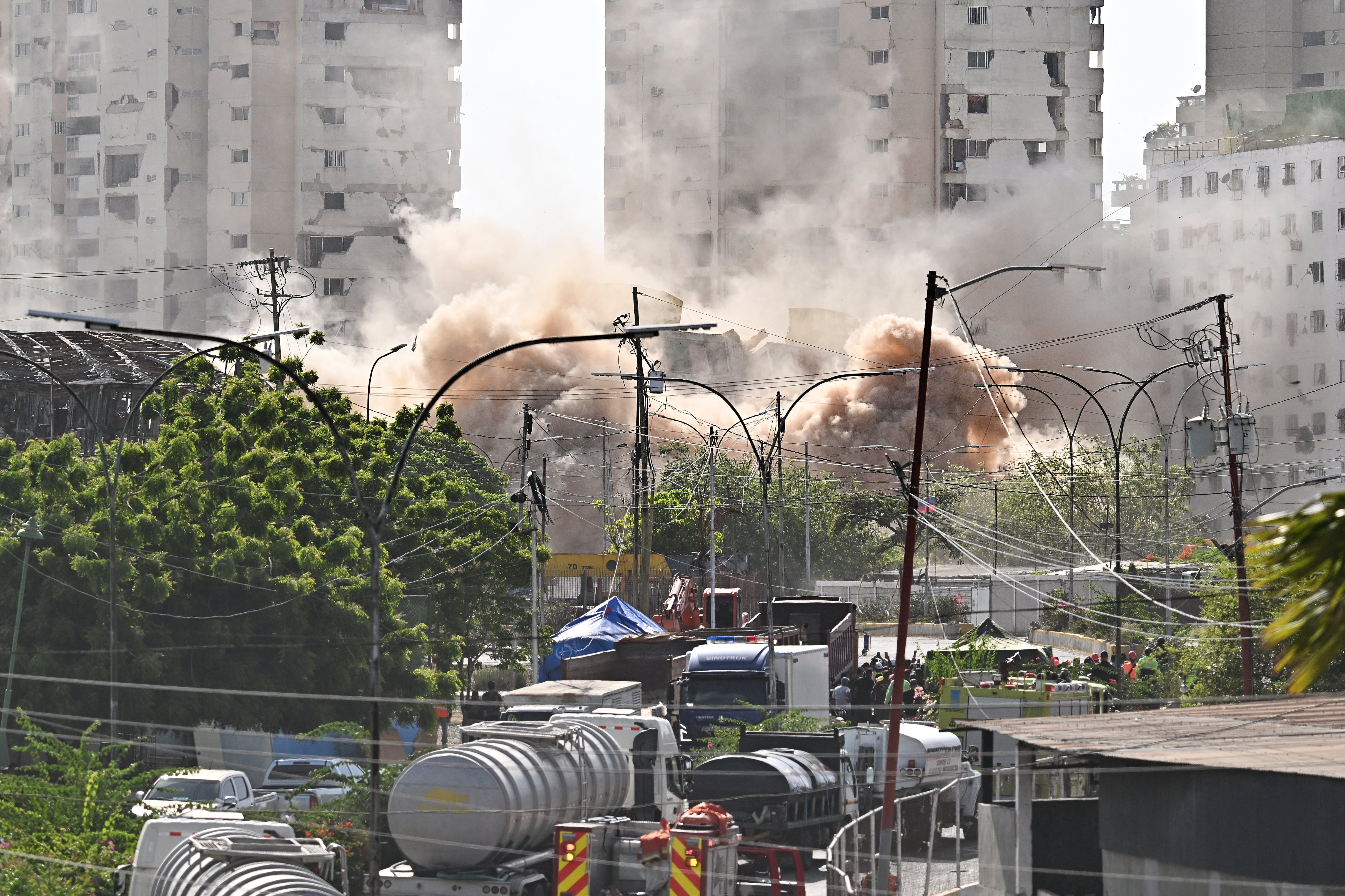 Edificios inestables son demolidos en La Guaira, Venezuela, un mes después del doble terremoto, mientras una densa nube de polvo cubre el área urbana y vehículos.