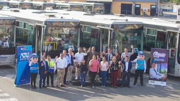 Un grupo de hombres, mujeres y dos mascotas posa delante de varios autobuses blancos y dos banners con logotipos de la ATU e Impulso Mujer