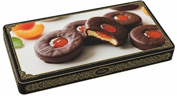 Caja rectangular oscura con decoración dorada. Galletas redondas cubiertas de chocolate con mermelada de albaricoque, una de ellas partida. Rodajas de albaricoque y una hoja.