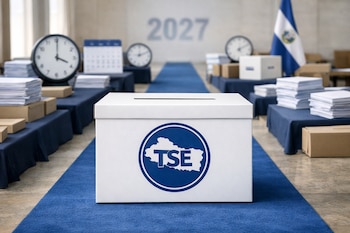 Urna electoral blanca del Tribunal Supremo Electoral de El Salvador sobre una alfombra azul, con relojes, calendarios, papeles y bandera de El Salvador al fondo.