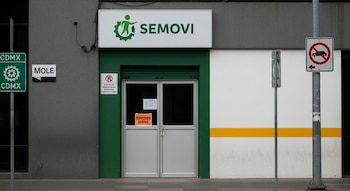 Fachada de un módulo de la SEMOVI en Ciudad de México con puerta cerrada y un cartel naranja de 'SUSPENDED SERVICE', junto a señales de tráfico urbanas.