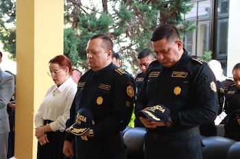 Dos agentes de policía en uniforme táctico cargan un ataúd gris adornado. Una fila de policías de uniforme blanco y azul saluda