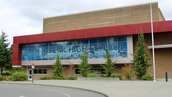 Vista exterior de la Glacier Peak High School, un edificio con fachada de ladrillo y paneles rojos, grandes ventanas y árboles verdes en el frente