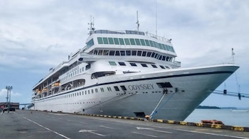 Un crucero blanco con el nombre Odyssey amarrado en un muelle asfaltado junto al mar