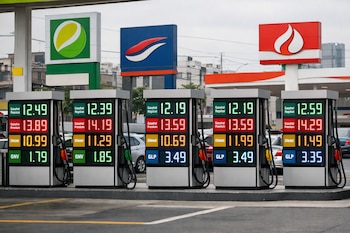 Surtidores digitales en una estación de servicio en Lima, Perú, muestran precios de gasohol, diésel, GNV y GLP. Varios autos y logos de marcas de combustible al fondo.