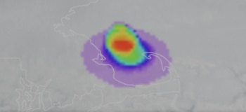 Mapa gris borroso con contornos de tierra blancos, cubierto por una gran forma ovalada de color púrpura, azul, verde, amarillo y rojo intenso en el centro