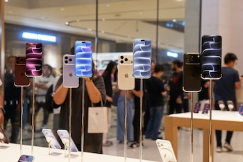 Varios teléfonos iPhone colocados sobre soportes metálicos en una tienda, con personas desenfocadas caminando al fondo