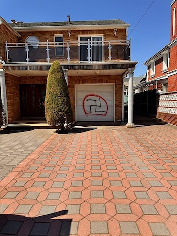Una casa de ladrillo con un garaje blanco. En la puerta del garaje, un grafiti de una esvástica negra dentro de un círculo rojo