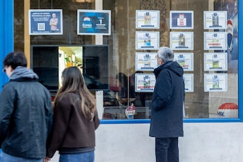 Un grupo de personas mira los anuncios de casas en venta en el escaparate de una inmobiliaria.