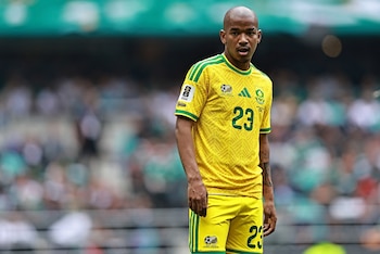 Hombre calvo, tez oscura, con camiseta y pantalón corto de fútbol amarillo y verde con el número 23. Fondo de estadio borroso
