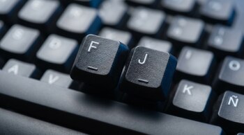 Primer plano de las teclas F y J de un teclado de computadora negro mate, con letras blancas. Ambas teclas muestran una raya en relieve central. El fondo está desenfocado.