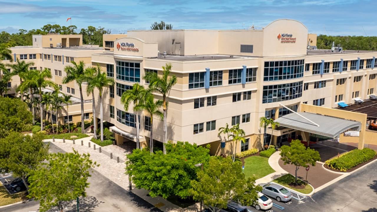 El edificio del hospital HCA Florida se alza entre palmeras y jardines verdes.