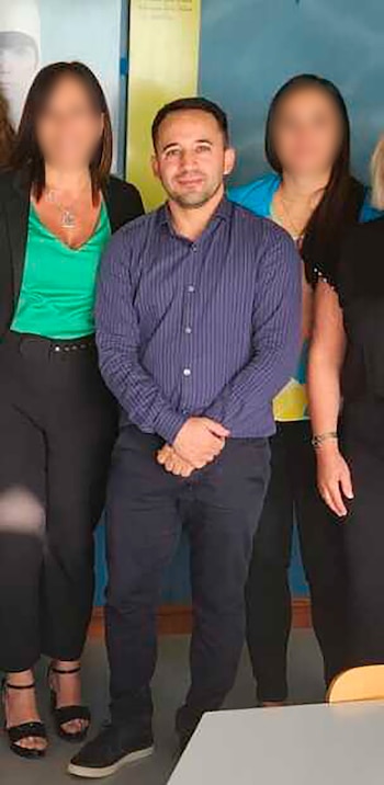 Un hombre de camisa azul de rayas y pantalones oscuros sonríe, flanqueado por dos mujeres con rostros borrosos. Fondo azul y amarillo claro