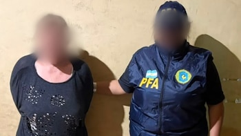 Una agente policial con uniforme azul y chaleco permanece junto a una mujer vestida de negro, ambas con los rostros difuminados