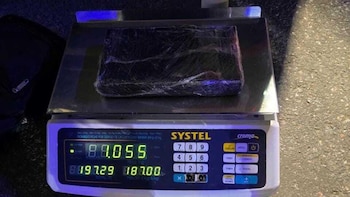 Un paquete rectangular oscuro envuelto en plástico sobre una báscula digital plateada con números verdes