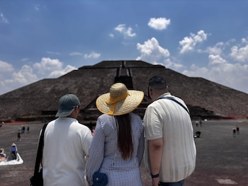 Vista trasera de tres personas, una con gorra, otra con sombrero de paja y la tercera con camisa clara, mirando una gran pirámide de piedra