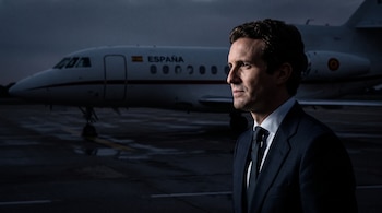 Pablo Casado viste traje y corbata en primer plano frente a un avión blanco con la bandera de España y la palabra España.