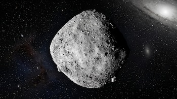 Un asteroide gris y rocoso en el centro sobre un fondo negro con estrellas, una galaxia espiral a la derecha y un cuerpo celeste a la izquierda.