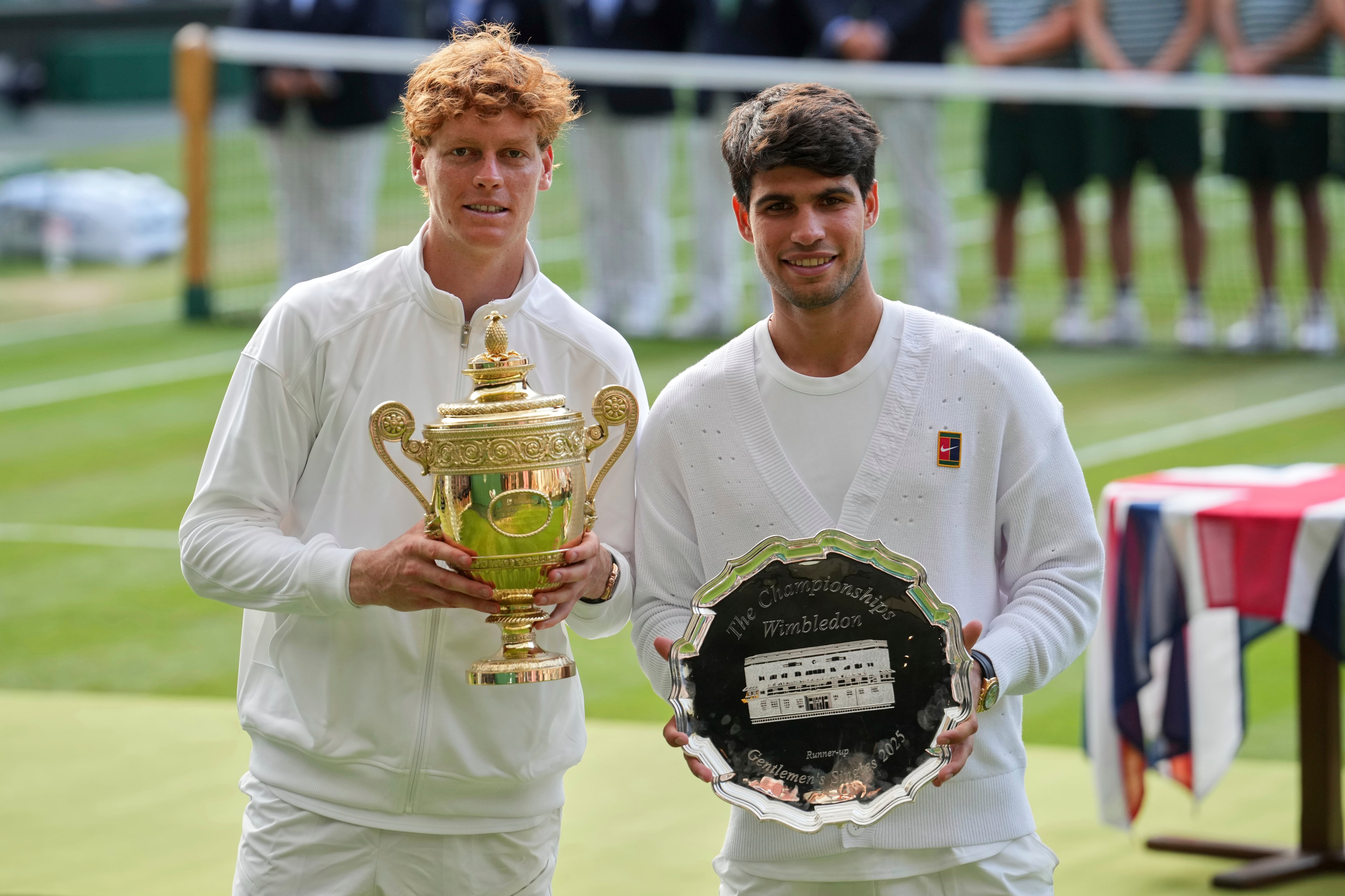 Jannik Sinner (izquierda) sostiene su trofeo de campeón tras derrotar a Carlos Alcaraz (derecha) en la final del torneo de Wimbledon, el 13 de julio de 2025, en Londres (AP Foto/Kin Cheung)