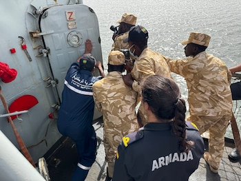 Personal militar español y mauritano en uniforme a bordo de un buque. Un hombre con uniforme azul trabaja en una puerta, otros en camuflaje observan