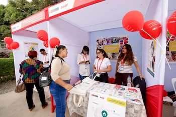 Varias personas conversan y observan folletos en un stand blanco y rojo con globos rojos y carteles de Inabif en un evento al aire libre