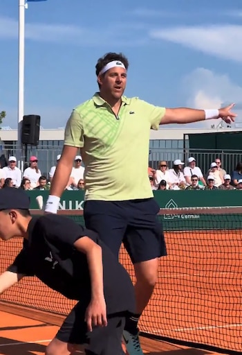 Juan Martín del Potro, con camiseta polo verde y vincha blanca, de pie en una cancha de arcilla, señalando a la derecha, con un recogepelotas agachado