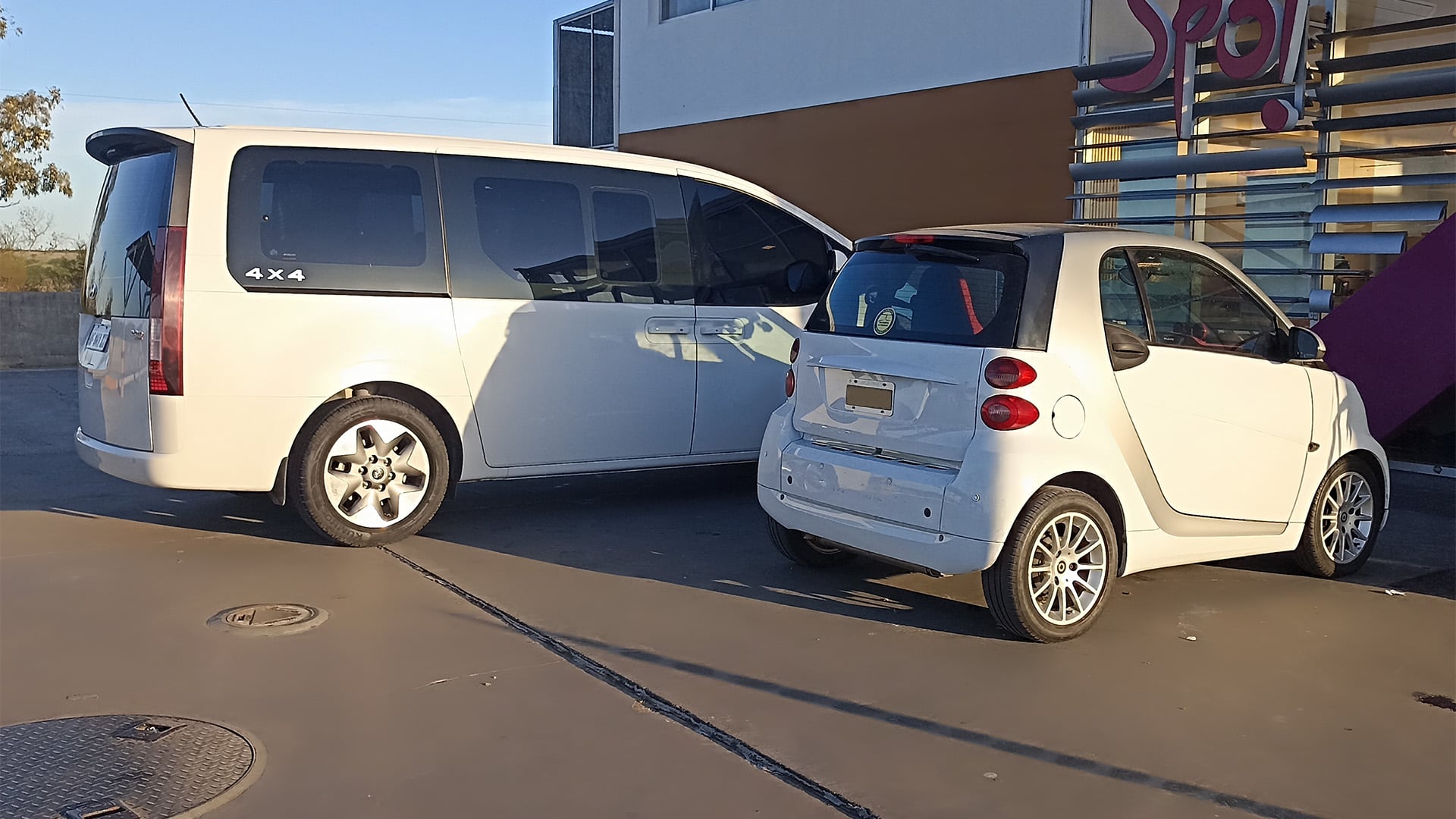 Un modelo Smart de 1998 estacionado junto a una van actual como muestra de la proporción de tamaño del pequeño auto que causó gran impacto tras su lanzamiento original.