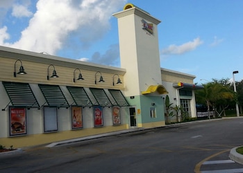 Vista exterior de un restaurante Sonic Drive-In con su torre de señalización y logotipo, estacionamiento y cielo azul con nubes blancas al fondo