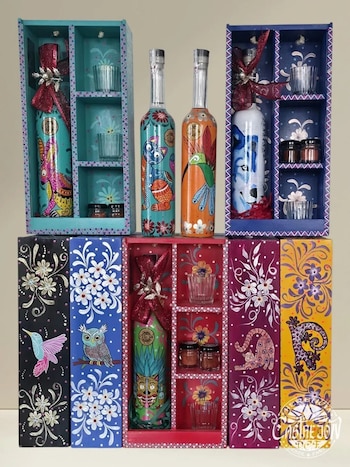 Seis cajas decoradas de madera con botellas de vidrio pintadas, copas pequeñas y frascos. Las botellas presentan diseños de animales y flores