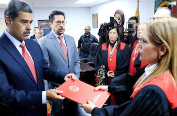 Nicolás Maduro, vestido de traje oscuro, pasa una carpeta roja a Cilia Flores, quien usa toga judicial. Otros funcionarios y cámaras están presentes