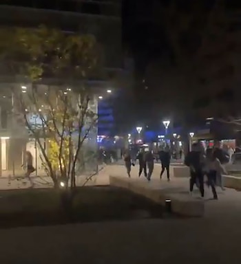 Vista nocturna del campus de la Universidad de Iowa con personas caminando y luces brillantes de edificios y farolas. Luces azules de emergencia visibles a distancia
