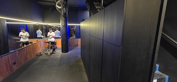 Imagen de un gimnasio con paredes oscuras y espejos, donde hombres con camisetas blancas usan sus teléfonos junto a equipos de ejercicio y pesas